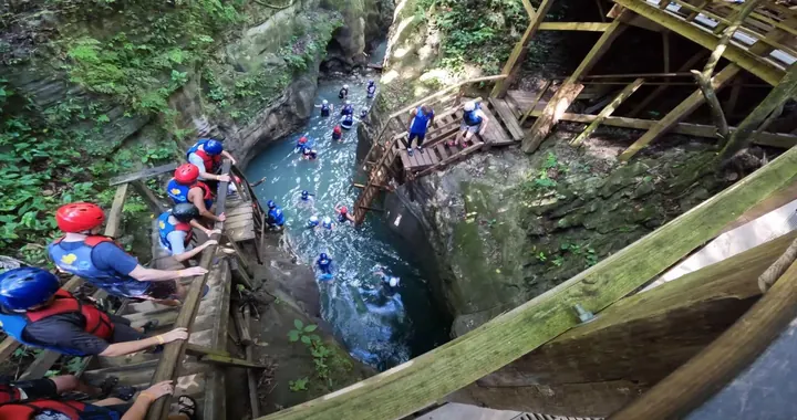 Visitors in helmets and life jackets climbing wooden stairs into a natural pool at the Damajagua waterfalls